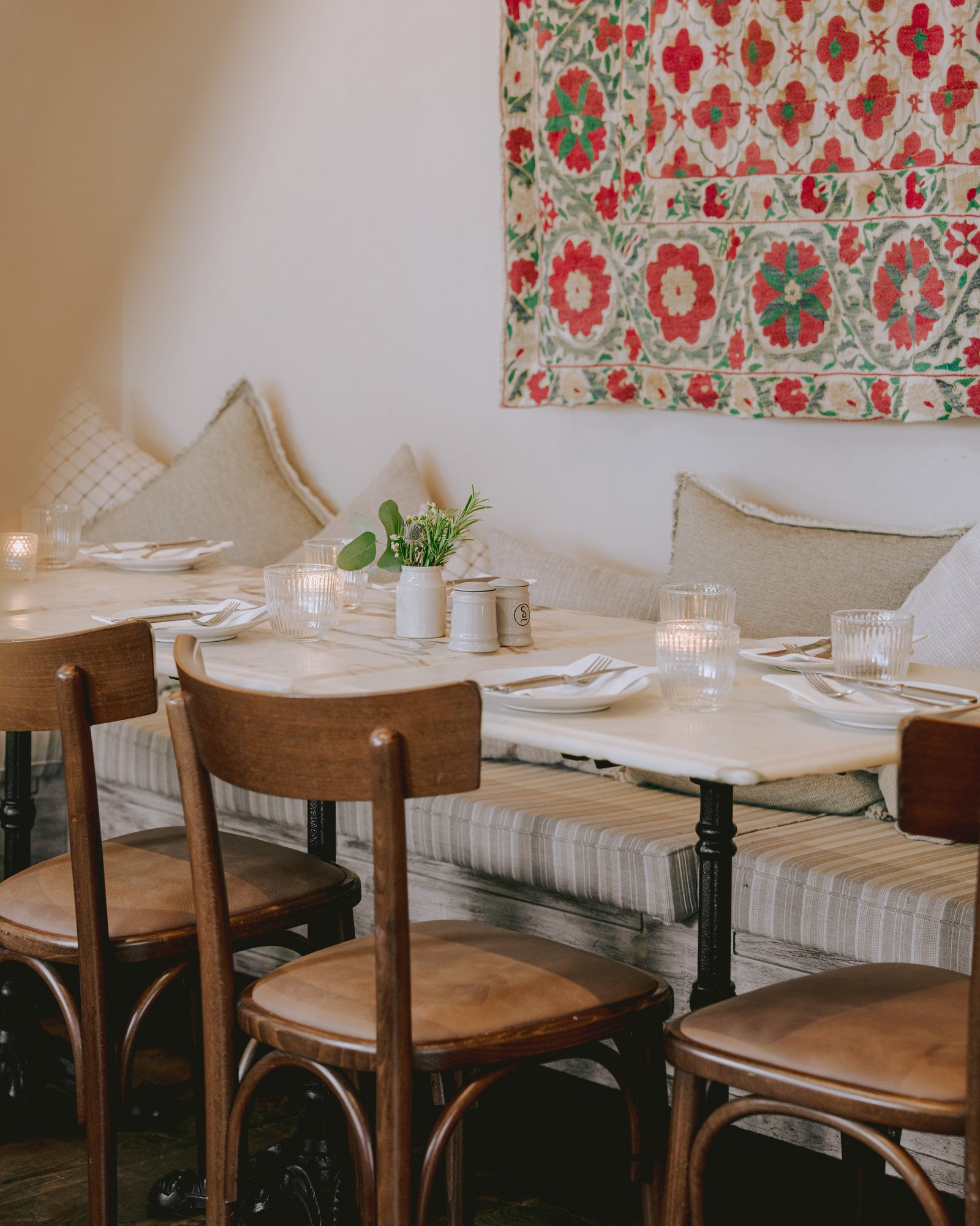 Villa Mamas London banquette with marble tables beneath a suzani textile
