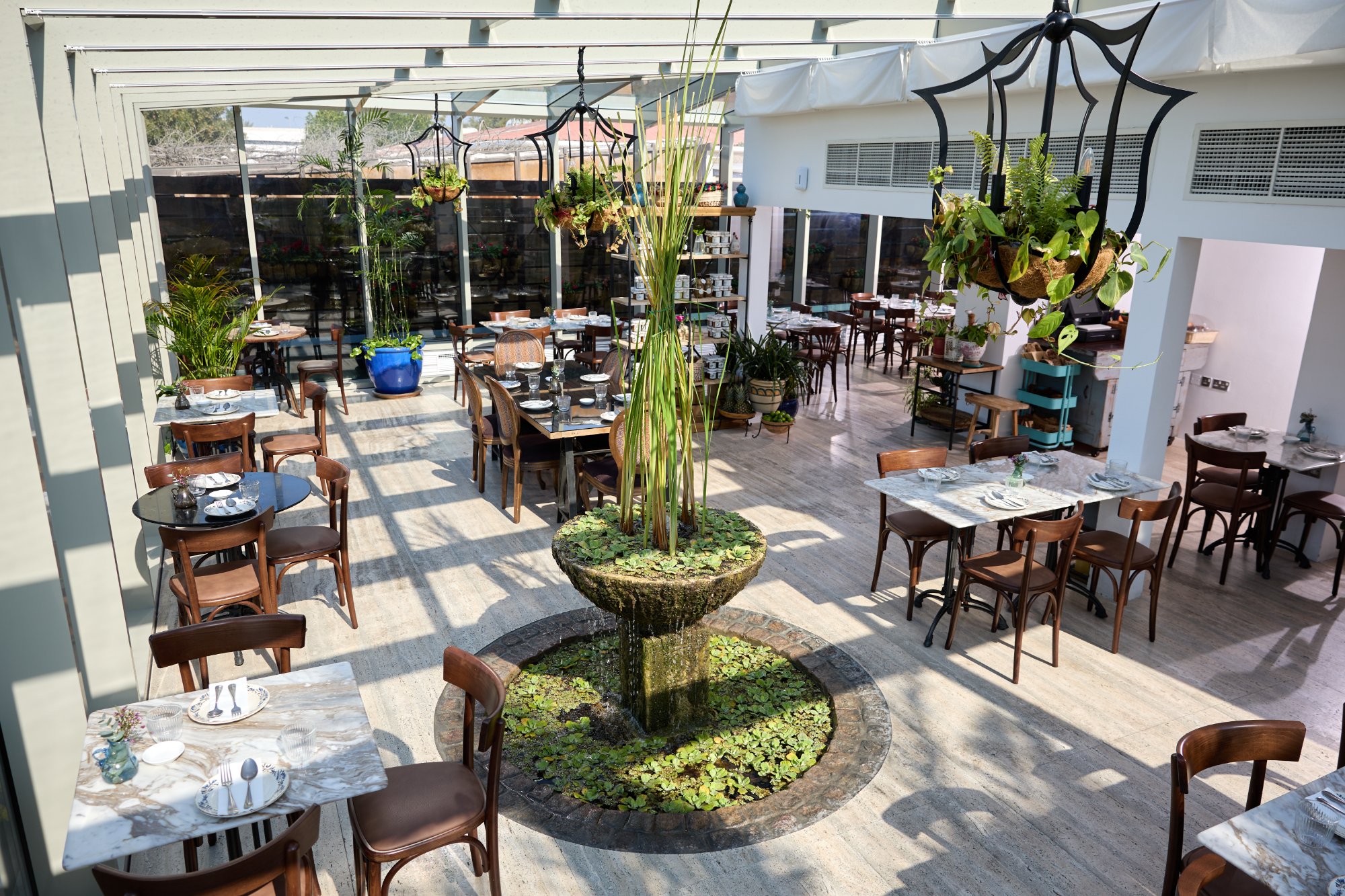 Villa Mamas Bahrain glasshouse dining room with a central fountain and hanging planters